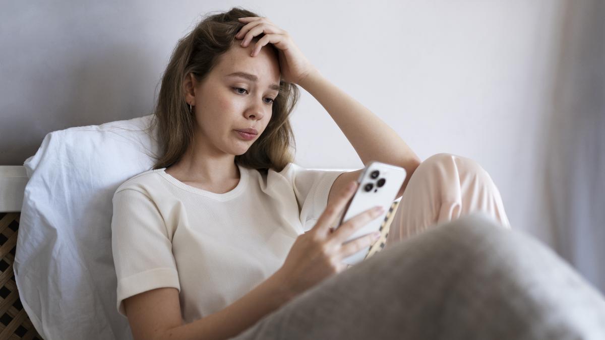 medium-shot-anxious-woman-laying-bed-with-smartphone_65438500