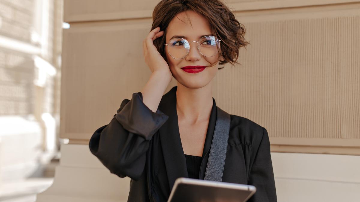 cute-woman-with-short-hair-red-lips-smiling-outside-cheerful-woman-with-red-lipstick-black-clothes-eyeglasses-holds-tablet-outdoors_79482200