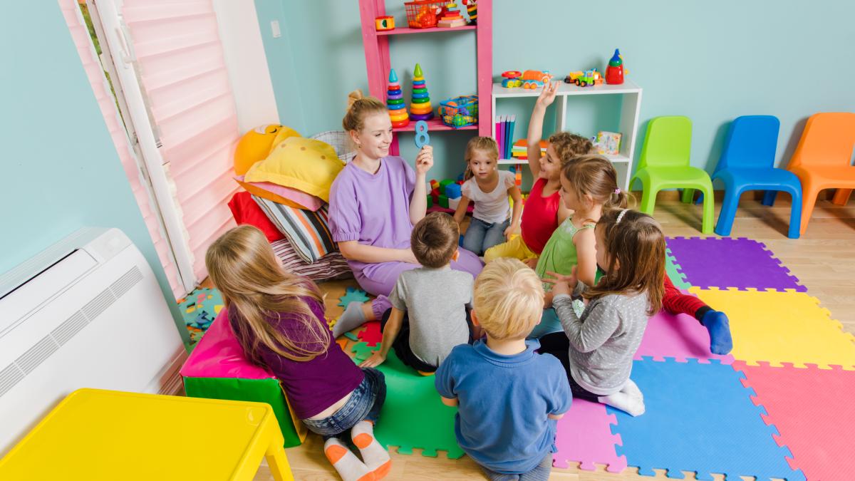 young-engaged-teacher-sitting-with-group-preschool-children-floor-lesson-process-learning-can-be-fun-room-with-colorful-mats-floor-multicolor-furniture_81934100