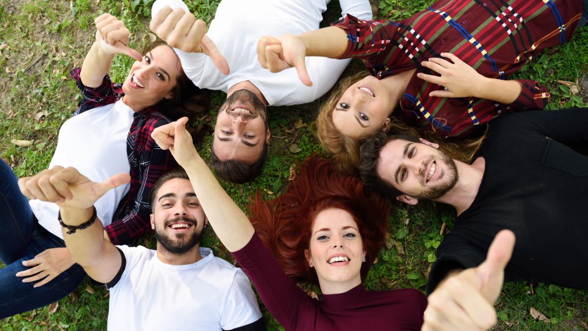 friends-with-thumbs-up-smiling-lying-lawn_87659800