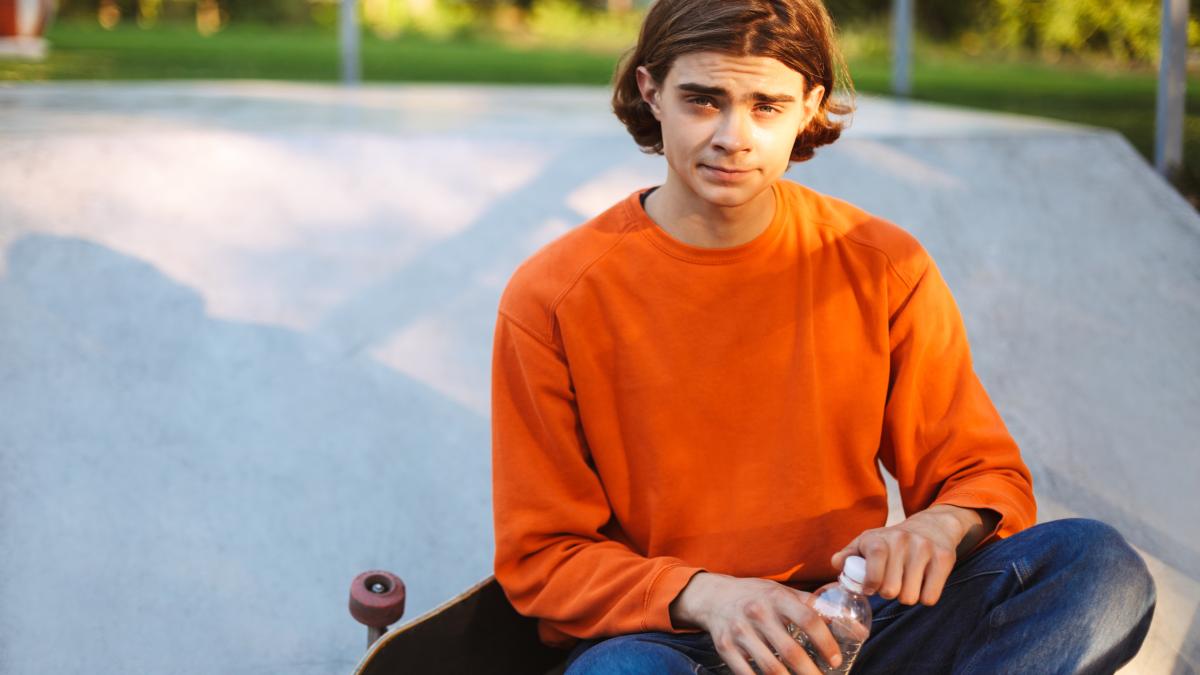 young-skater-orange-pullover-holding-bottle-water-hands-while-dreamily-looking-camera-with-skateboard-skatepark_68963300