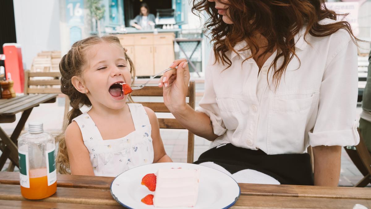 young-mom-eating-cake-with-smiling-kid-street_22065400