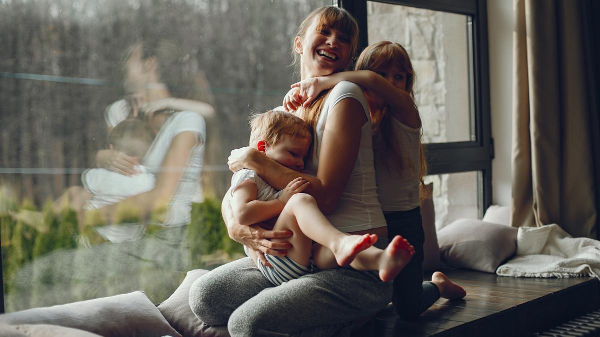 mamă cu doi copii în brațe, zâmbind